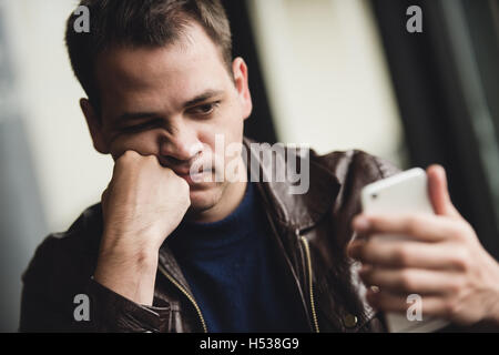 Portrait of tired young businessman typing on cellphone at cafe Stock Photo