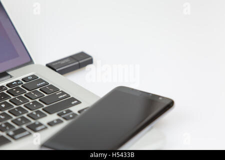 a black usb stick plugged on the right side of laptop. closeup shot with focus on keyboard and usb stick. a smartphone lying on  Stock Photo