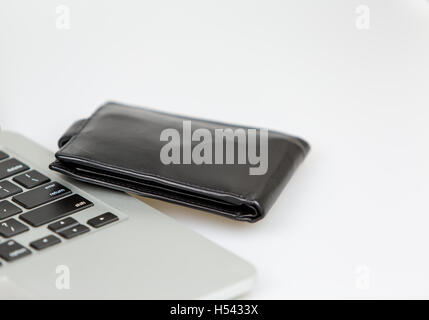 black leather wallet lying beside a laptop on a desk. studio shot on a white background. closeup Stock Photo