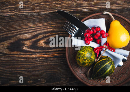 Rustic autumn place setting, ceramic plate, knife and fork wrapped with napkin on rustic wooden table, top view, Thanksgiving Stock Photo