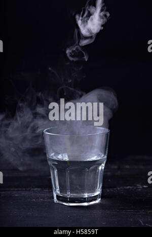 Hot water with a lot of steam in a glass at a black background. Dark photo Stock Photo