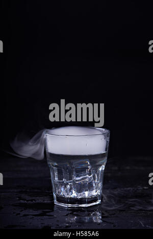 Hot water with a lot of steam in a glass at a black background. Dark photo. Concept photo: three state of water - ice, water, st Stock Photo