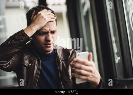 Bad news. Depressed young man expressing negativity while reading message on the mobile phone Stock Photo