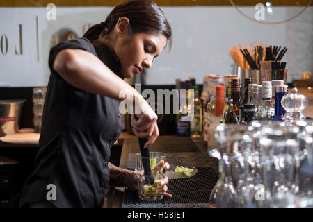 Female bartender mixing a cocktail, crushing the lemons Stock Photo
