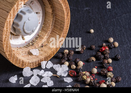 Pepper Mill, Sea Salt and Pepper Grains on Dark Stone Surface Close Up Stock Photo