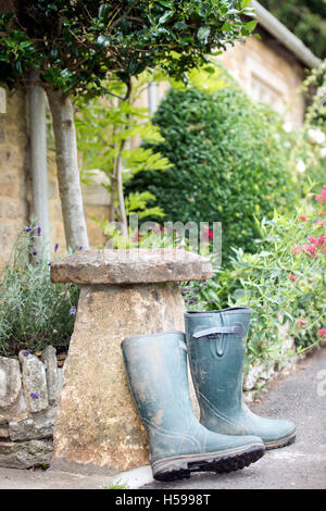 A pair of wellington boots leaning against a staddle stone outside a Cotswold country cottage, UK Stock Photo