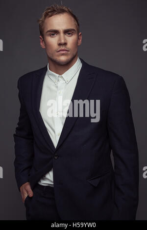 elegant young fashion man in tuxedo looking at the camera while holding his hands on his jacket and a leg behind the other Stock Photo