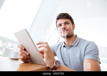 Smiling casual businessman holding tablet and looking away indoors Stock Photo