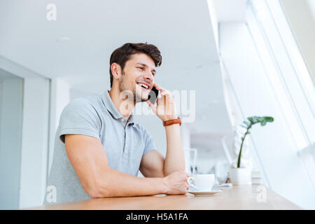 Cheerful casual man talking on cell phone while having coffee break indoors Stock Photo