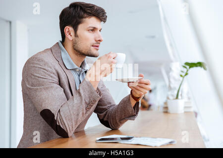 Casual young pensive businessman drinking coffe while sitting in cafe Stock Photo