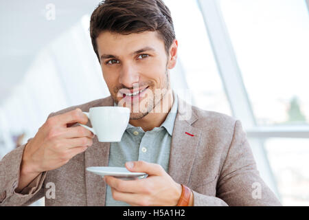 Happy smiling businessman in jacket drinking coffee indoors and looking at camera Stock Photo