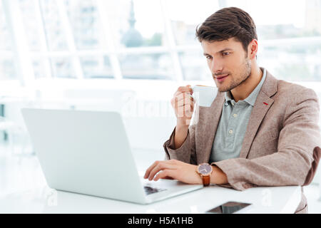 Handsome young businessman having cup of coffee and using laptop indoors Stock Photo