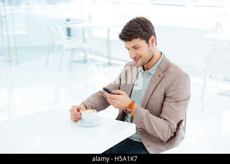 Smiling young businessman typing message on smartphone while sitting indoors Stock Photo