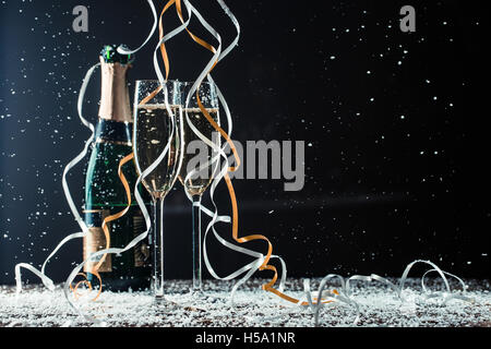 Champagne bottle, glasses on table covered snow and cascading ribbons Stock Photo