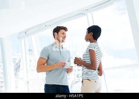 Two young business people standing and talking in office during coffee break Stock Photo