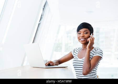Smiling african american young woman accountant using laptop and smartphone in office Stock Photo