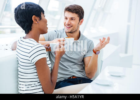 Cheerful young man sitting in cafe and drinking coffee with young african woman Stock Photo