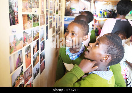 Two East African Ugandan children stare at a wall of photographs in their rural Ugandan school with happiness on their faces Stock Photo