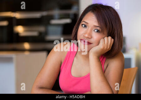 portrait of beautiful hispanic woman sitting at table and looking sad at camera Stock Photo