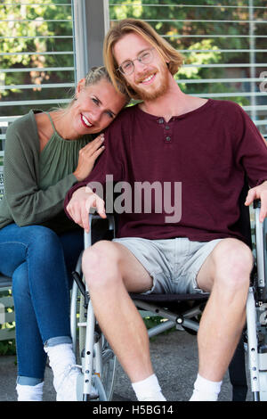 woman hugging young man sitting in wheelchair and smiling Stock Photo