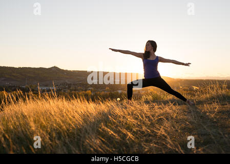 Woman doing yoga warrior II pose during sunset Stock Photo