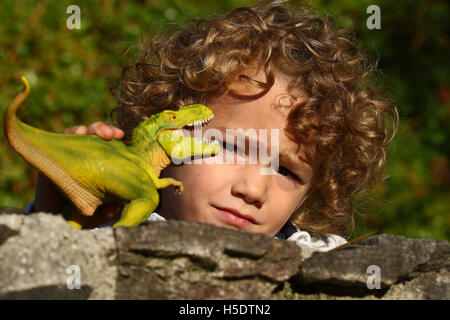Young boy playing with toy dinosaur on granite wall against a blurred green background Stock Photo