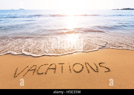 Vacations text written in the sand of a tropical beach with beautiful sunset in the background Stock Photo