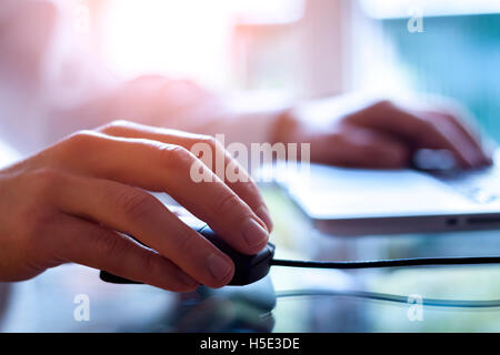 Male hand holding computer mouse with laptop keyboard in the background Stock Photo