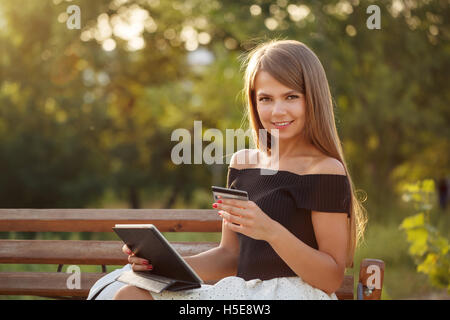 Cute girl holding a tablet pc and credit card. Payment for online purchases. Banking online. Girl smiling Stock Photo