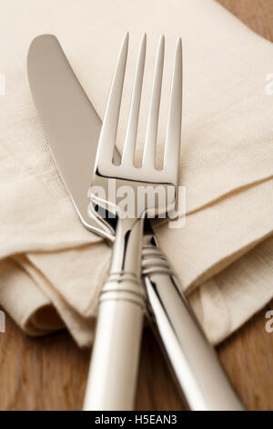 Simple, classic table setting place setting with high quality silverware fork and knife on white linen napkin. Stock Photo