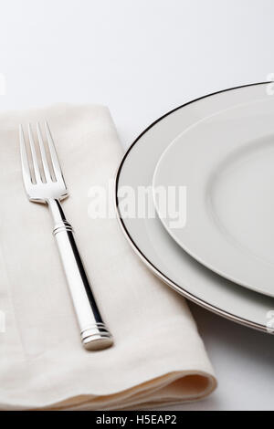 Fine dining table setting place setting with high quality classic style white china dishes, linen napkin and silverware fork. Stock Photo