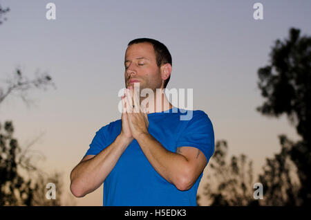 Man praying alone at dusk in an outdoor park. Stock Photo