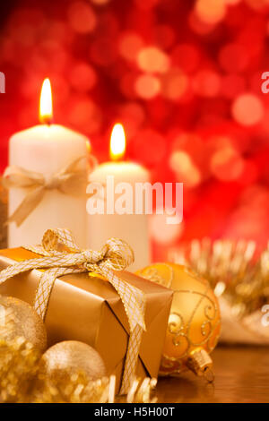 Red and golden Christmas baubles, a gift and candles in front of defocused red lights. Stock Photo
