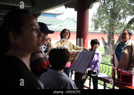 A young Chinese woman sings and smiles having fun conducting her friends, they do it for leisure in the Temple of Heaven Park Stock Photo