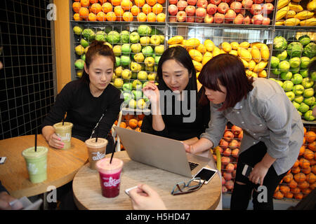Two young Chinese women look at the work the third one did on the her laptop, one is even trying to help, smartphones are seen. Stock Photo