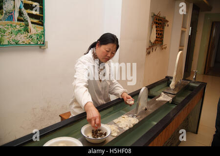 Woman separates the dead caterpillar from the wet cocoon. She will stretch the cocoon to fabric on the metal arches. A traditional silk factory. China Stock Photo