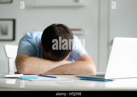 Portrait of a man lying down at desk near laptop Stock Photo