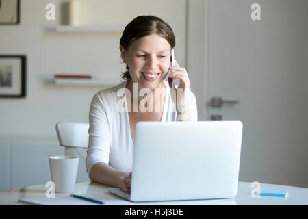 Portrait of smiling woman near laptop talking on the phone. Stock Photo