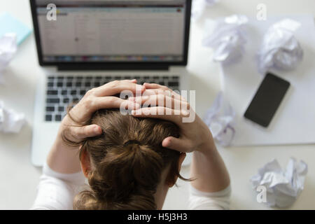 Portrait of a woman grabbing head at desk near the laptop Stock Photo