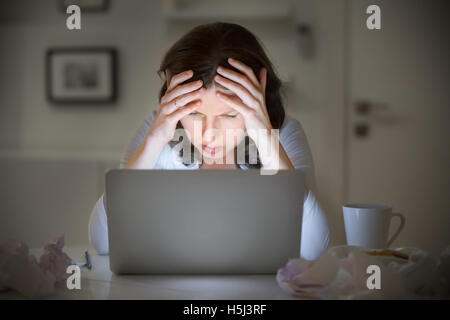 Portrait of a woman grabbing her head near the laptop Stock Photo