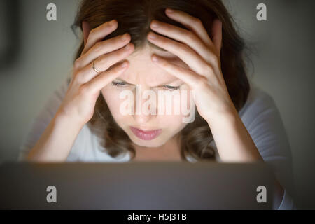 Portrait of a woman grabbing head near laptop, late at night Stock Photo