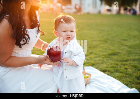Mother giving fresh red apple to her little daughter in park Stock Photo