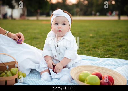 Cute little girl sitting and hiding big red apple on picnic in park Stock Photo