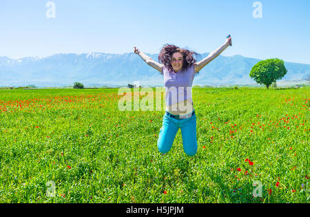 The young girl jumps on the poppy field and laughs, Samarkand suburb, Uzbekistan. Stock Photo