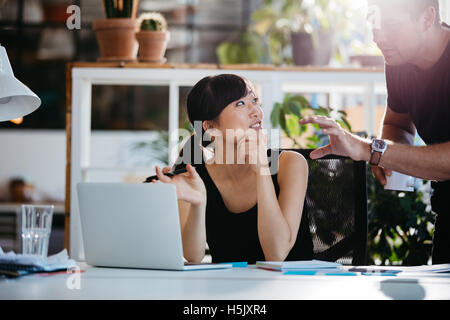Smiling businesswoman talking with partner while sitting at her desk. Professional employees discussing ideas of project on lapt Stock Photo
