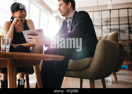 Shot of two young businesspeople using digital tablet in lobby of modern office. Man and woman sitting on foyer working together Stock Photo