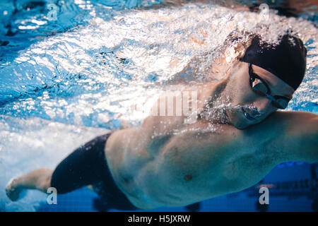 Professional male swimmer inside swimming pool. Underwater shot of fit young man practising in pool. Stock Photo