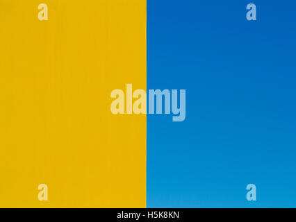 An architectural abstract image with a bright yellow wall bisecting the frame and a clear blue sky on the other half. Stock Photo