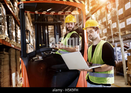 Workers using technology and forklift in warehouse Stock Photo