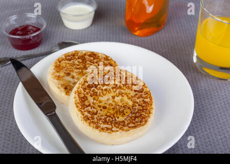 Crumpets on a plate with maple syrup and orange juice on the breakfast table Stock Photo